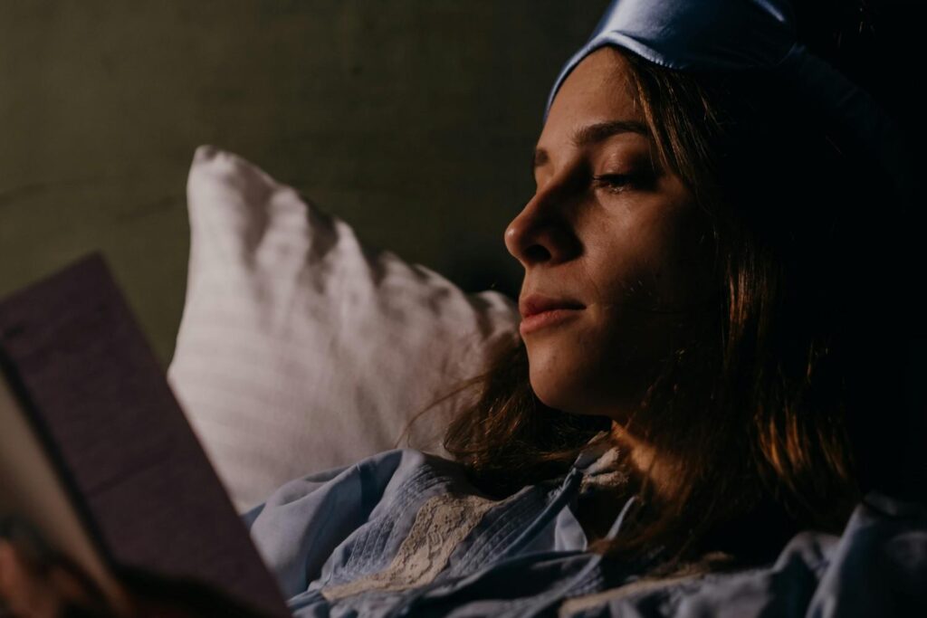 woman reading in low light to create a calming mindset before sleep.